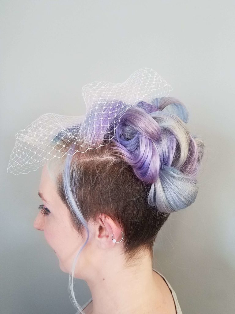 A pastel lilac and blue updo, pinned and finished with a birdcage veil.