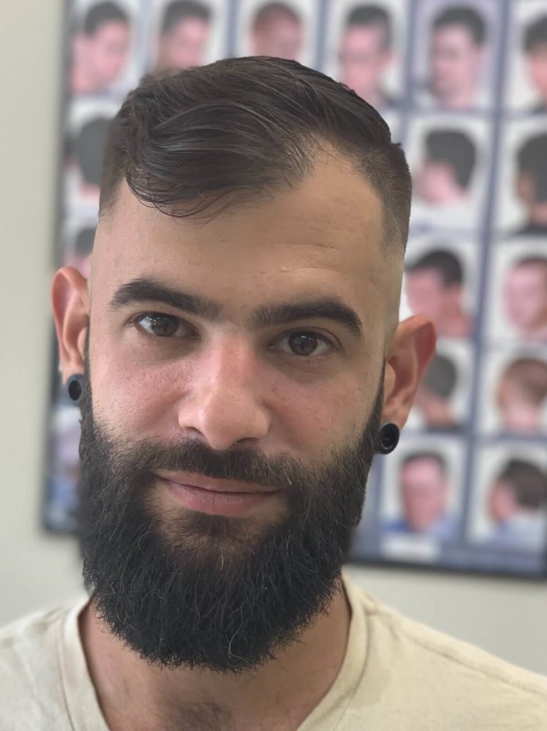 A high skin fade with a side part, and a full beard shaped along the jaw.